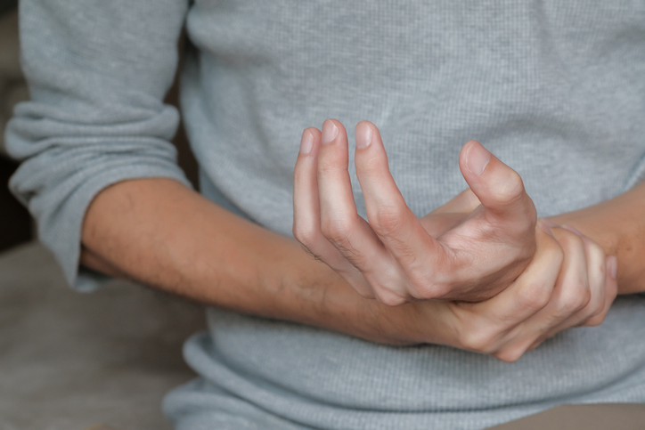 Man holding hand with muscle weakness, numbness and paralysis symptom